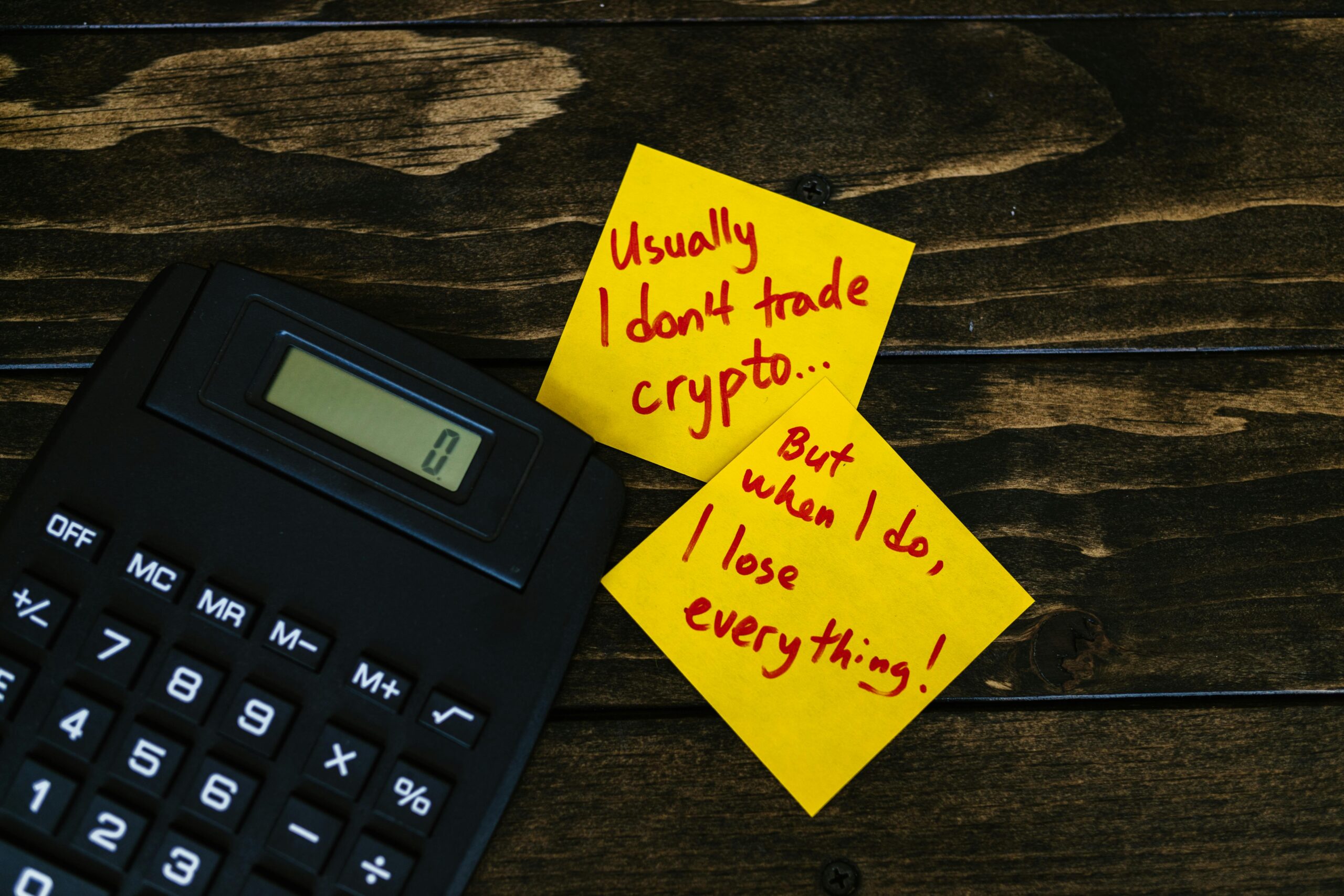 Funny sticky notes about cryptocurrency trading with calculator on wooden table.